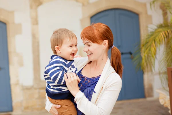Jonge glimlachend moeder bedrijf glimlachend baby jongen in de gestreepte jac — Stockfoto