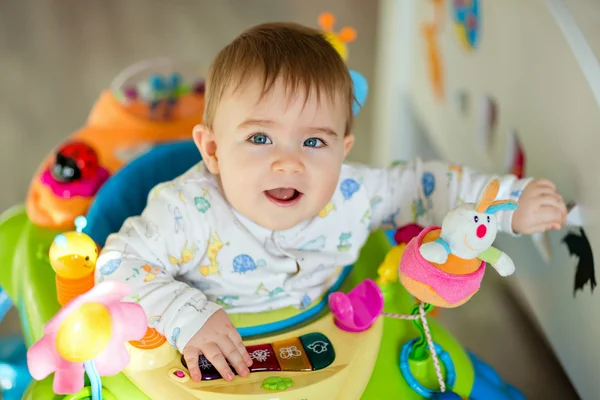 Liten pojke sitter i en färgglada baby Walker med leksaker och leende hemma i barnkammaren, närbild — Stockfoto