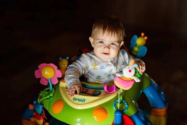 Kis baba fiú ül világos Walker és a nap süt, ház sötét háttér előtt — Stock Fotó