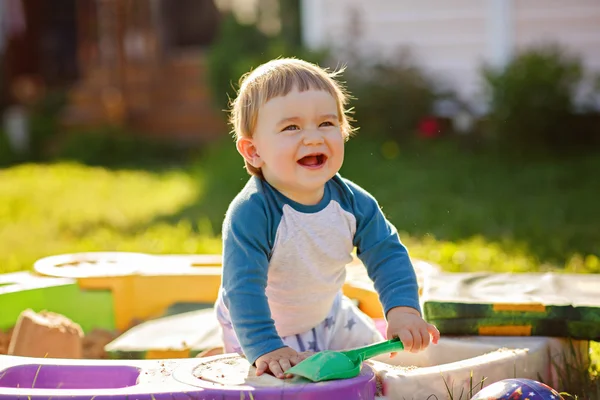 Kleine mollig babyjongen lacht, zitten in de zandbak in de zomer bij mooi weer — Stockfoto