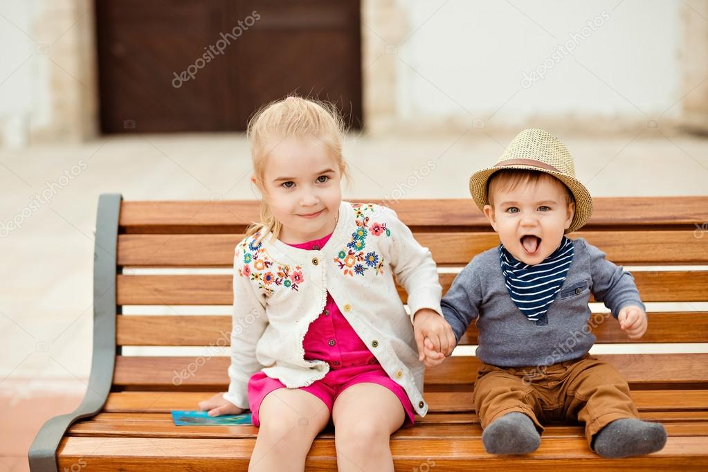 Beautiful girl holds the hand of brother laughing baby boy in a 