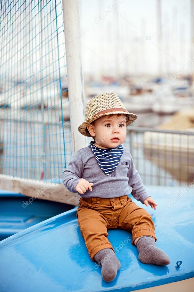 Little adorable baby boy in a straw hat and brown pants sitting 