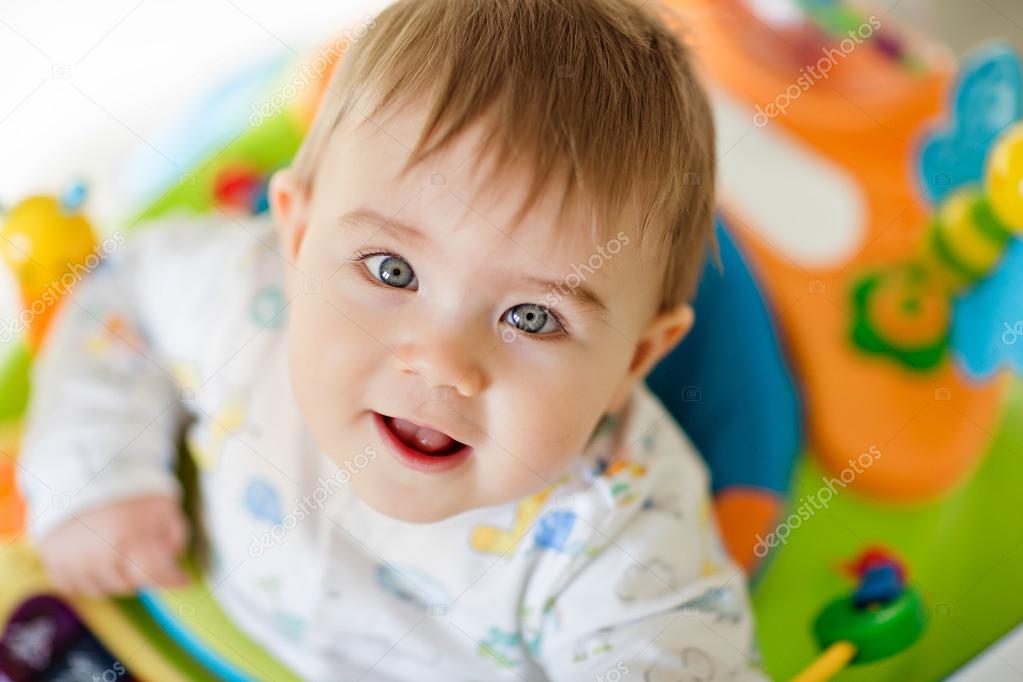 Little baby boy sitting in a colourful baby Walker with toys and   smiling at home in the nursery, close-up