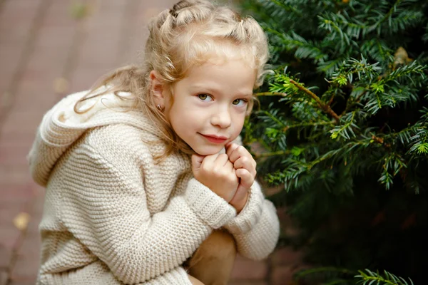 Schattig klein krullend blond meisje in beige gebreide trui glimlacht — Stockfoto