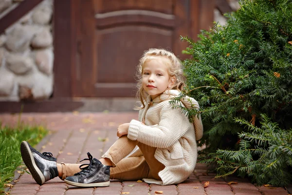 Adorable little curly blond girl in beige knitted sweater smilin — ストック写真