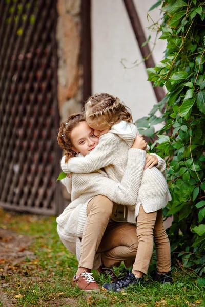 Two charming sisters in the same curly beige knitted sweater emb — Stock Photo, Image