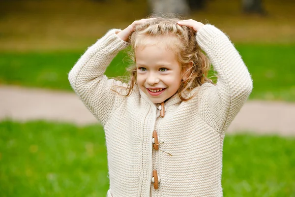 Adorável pouco encaracolado menina loira em bege malha suéter sorrisos — Fotografia de Stock