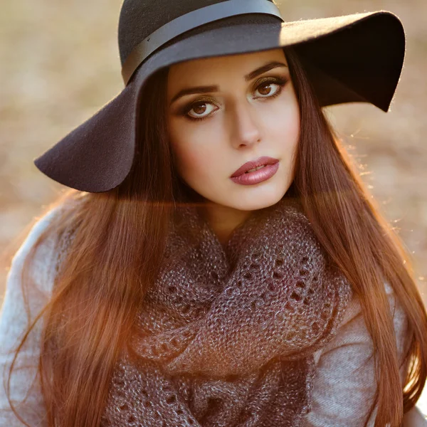 Porträt einer sehr schönen jungen brünetten Frau mit glänzenden glatten Haaren in grauem Mantel und schwarzem Hut, die vor dem Hintergrund der herbstlichen Landschaft im Park lächelt, Nahaufnahme — Stockfoto