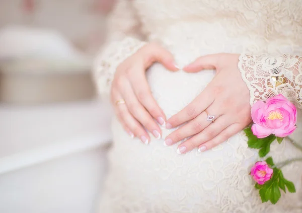 Zwangere vrouw die haar handen in de vorm van een hart op haar buik — Stockfoto