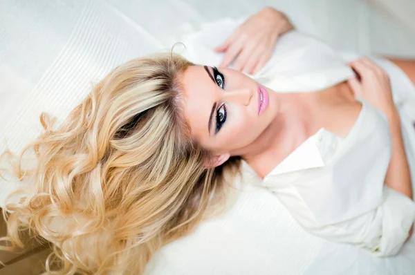Porträtt av sexiga blonda flickan i vit skjorta ligger på sängen på — Stockfoto