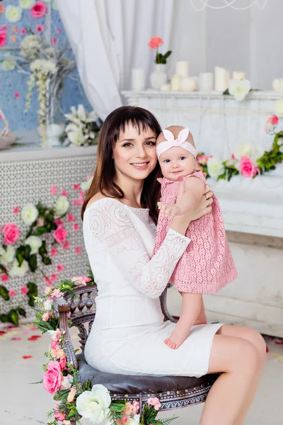 Beautiful and happy mom brunette in a white dress holding on the — Stock Photo, Image