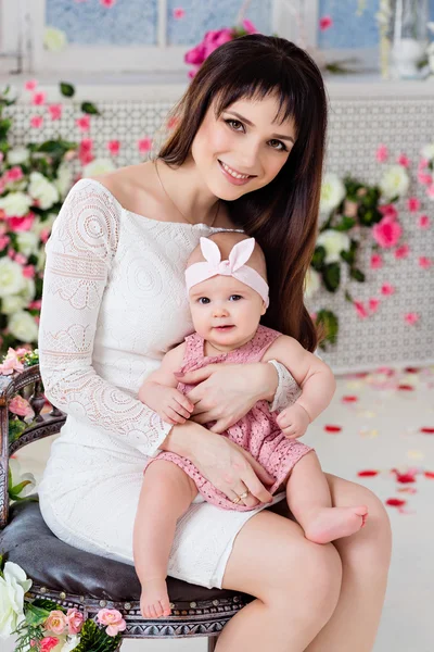 Beautiful and happy mom brunette in a white dress holding on the — Stock Photo, Image