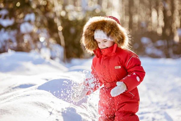 Μικρό πολύ χαριτωμένο κορίτσι σε ένα κόκκινο κοστούμι με κουκούλα γούνα παίζει με το χιόνι — Φωτογραφία Αρχείου