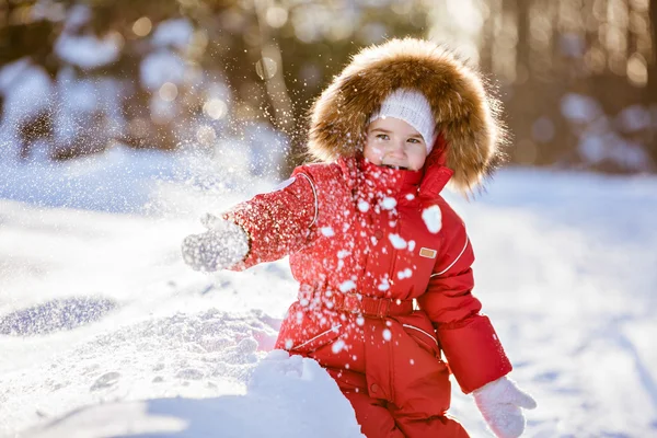 Piccola ragazza molto carina in un abito rosso con cappuccio di pelliccia getta neve in — Foto Stock