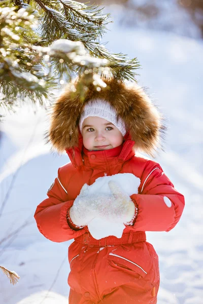 Small very cute girl in a red suit with fur hood keeps the snow — Stock Photo, Image