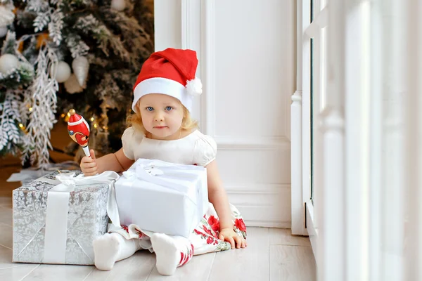 Petite fille charmante blonde dans un chapeau de Père Noël, souriante et assise — Photo