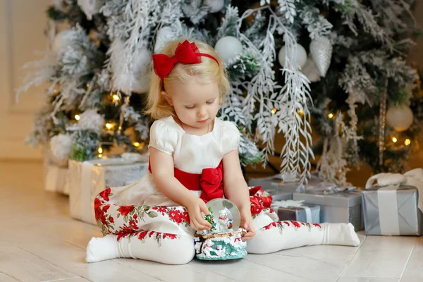 Babymeisje charmante blonde in een rode jurk zitten naast een — Stockfoto