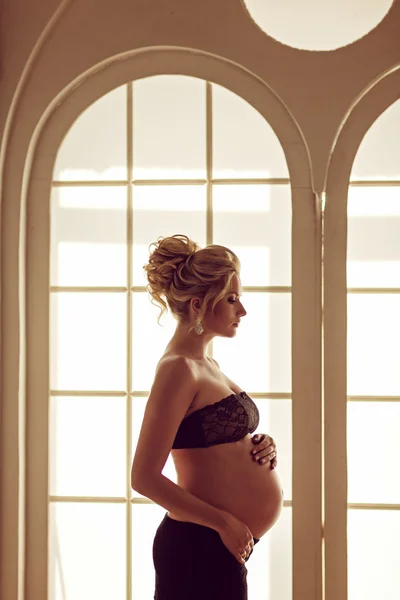 Beautiful pregnant blonde in a black skirt and lace top holds th