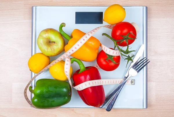 Peppers, tomatoes, apple and lemons on a scale with cutlery and t