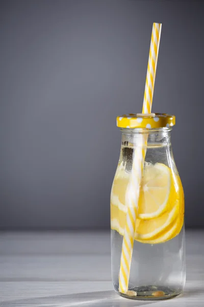 Botella amarilla de limonada con limones y paja . — Foto de Stock