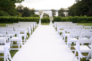 Minimalist düğün hazırlığı kavramı: beyaz sandalyeler ve banklar düğün kemerine giden güzel bir kompozisyonda düğün töreni için bir koridor oluşturur.