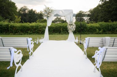 Minimalist düğün hazırlığı kavramı: beyaz sandalyeler ve banklar düğün kemerine giden güzel bir kompozisyonda düğün töreni için bir koridor oluşturur.