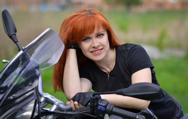 Mutlu, neşeli, gülümseyen kız olsun, yeni modern siyah motosiklet satın almak. Sevimli, güzel bir gülümseme ile kızıl saçlı kız büyük, siyah motosiklet üzerinde oturup. Siyah eldiven ve t-shirt bisiklet yalın profesyonel bisikletçi.
