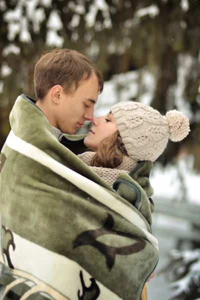 Hombre feliz besando a su hermosa chica en la frente y cubre su manta. Un hombre guapo besar en la frente su amada, hermosa, chica bonita con suéter, manoplas y cabaña . —  Fotos de Stock