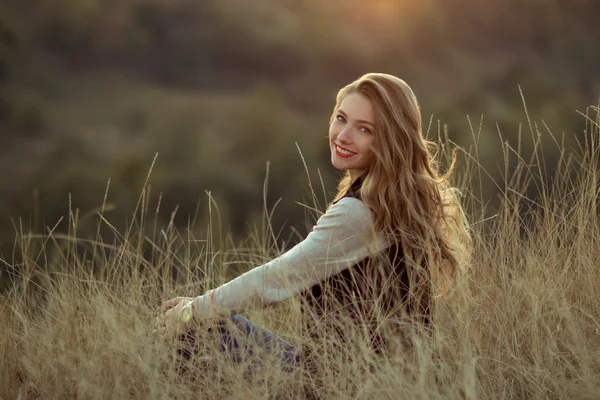 Ragazza carina sorridente con meraviglioso, carino, sorriso bianco e labbra rosse guardare il tramonto, sedersi sulle colline, in montagna in estate.Divertitevi sorridente allegra ragazza allegra con bel sorriso sedersi sulle colline e osservare il tramonto — Foto Stock