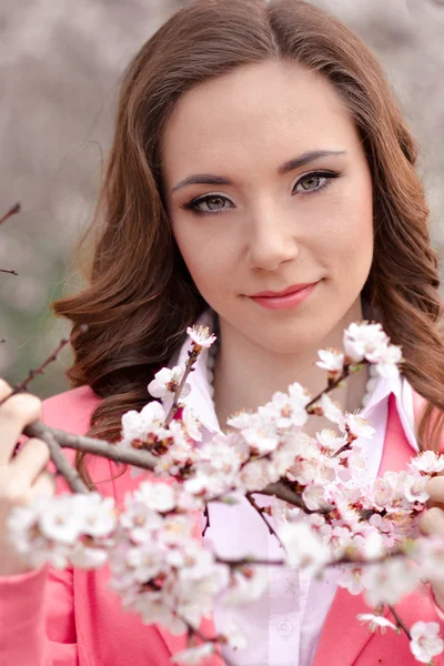 春の庭で木々を咲かせる非常に美しい女の子。春だ非常にかわいい、素晴らしい、ゴージャスな、完璧な髪型を持つ素敵な女の子、多くの白い花と春の開花公園のピンクのジャケット。かわいい. — ストック写真