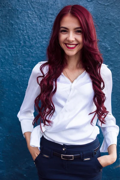 Portrait de rousse, rehead fille souriante et souriante aux cheveux roses. Heureux client juste de coiffeur et coiffeur. Une belle femme rousse ardente aux cheveux parfaits avec un fond abstrait bleu. Une photo de beauté d'un jeune aux yeux foncés — Photo