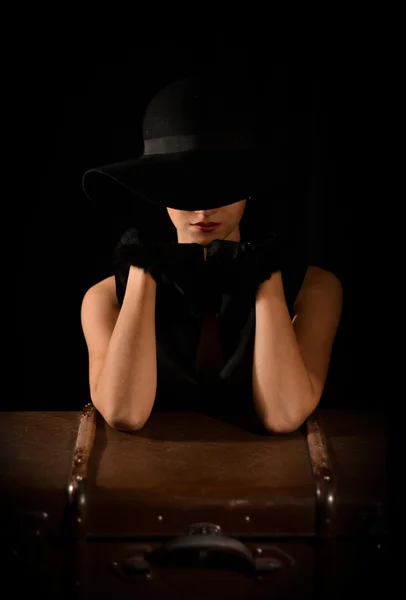 Photo de mode de belle dame au chapeau noir élégant. Magnifique, attrayant, sensuel, élégant, fille classique, modèle en robe noire, gants noirs assis sur chaise noire sur fond noir avec sac . — Photo