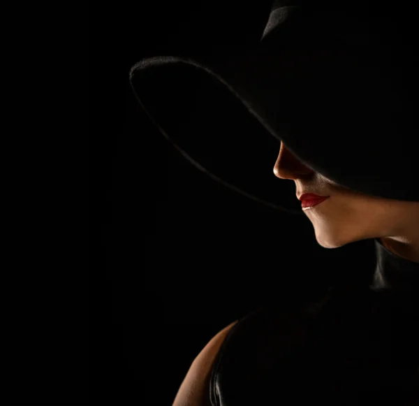 Fashionable shot of beautiful profile, silhouette with a mole, red lips, black hat and dress on black background in studio. Royalty Free Stock Images