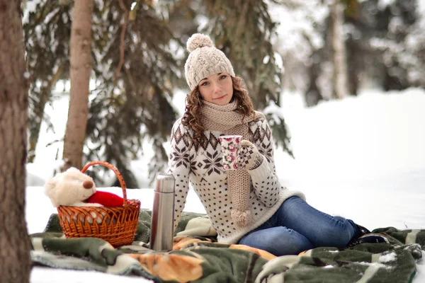 Beautiful girl sitting on a blanket in the winter in the forest, fosest and drinking tea, has good, fun, funny, happy time, date, picnic. — Stockfoto