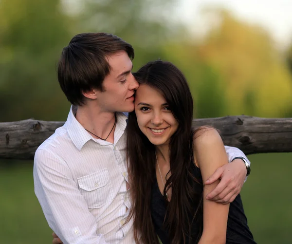Handsome,happy boy,man kisses her beloved,enamoured,beautiful,attractive,smiling,cheerful girl,woman on the forehead.Couple have a good,wonderful rest,weekend, romantic date outdoors in summer, spring. Man,boy hug, embrace his lovely,cute girl,woman. — Stock fotografie