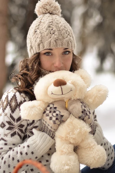 Linda, agradável, sorridente, pouco e vestindo cabana de camisola e mitenes e menina com um ursinho de pelúcia na floresta de inverno.Retrato de menina adorável com bonitinho, brinquedo agradável.Bonito, bonito, menina agradável abraçar um urso de pelúcia fofo, branco, bege. Menina e urso no inverno — Fotografia de Stock