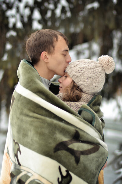 Happy man kissing his beautiful girl on the forehead and covers her blanket. A handsome man kiss on the forehead her beloved, beautiful, pretty girl with sweater, mittens and hut.