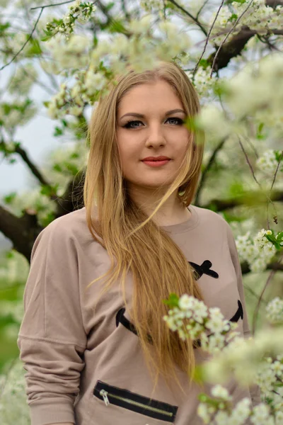 Rubia, de lujo, agradable, chica bonita con el pelo largo, brillante, brillante, sano de pie en el jardín verde floreciente primavera con flores.Cute, agradable, bonita, atractiva, hermosa chica con el pelo largo, rubio, recto en el jardín floreciente en primavera . —  Fotos de Stock