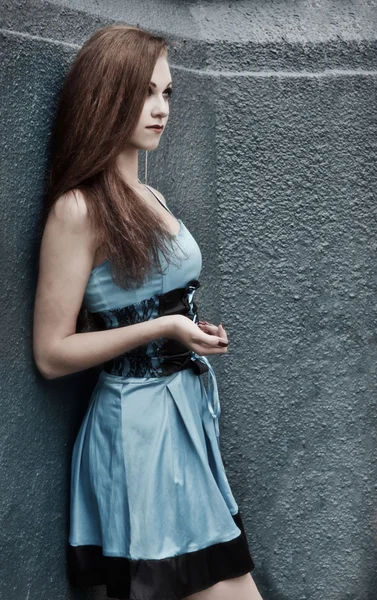 Sexy, sexual, fashionable, glamorous, serious, snorting, stunning, excellent, awesome, attractive, beautiful in short blue dress standing near the stone gray wall.