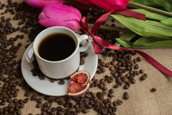 Taza de café con frijoles crudos en arpillera con tulipanes rosas — Foto de Stock