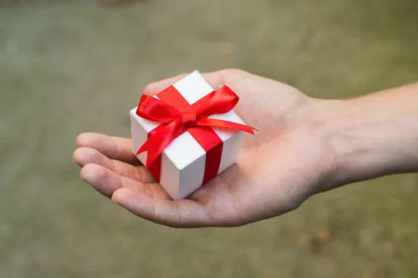 Weiße Geschenkschachtel mit roter Schleife in den Händen des Mannes — Stockfoto