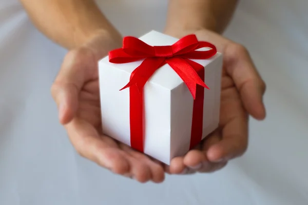 Beyaz hediye kutu kırmızı kurdele ile holding adam eller