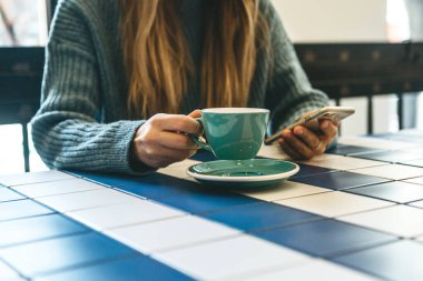 Bir kız kafede sıcak çay ya da kahve içer ve cep telefonu ya da cep telefonu kullanır..