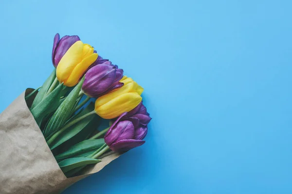 Hermosos tulipanes de primavera amarillos y morados sobre fondo azul claro. Espacio para texto. — Foto de Stock