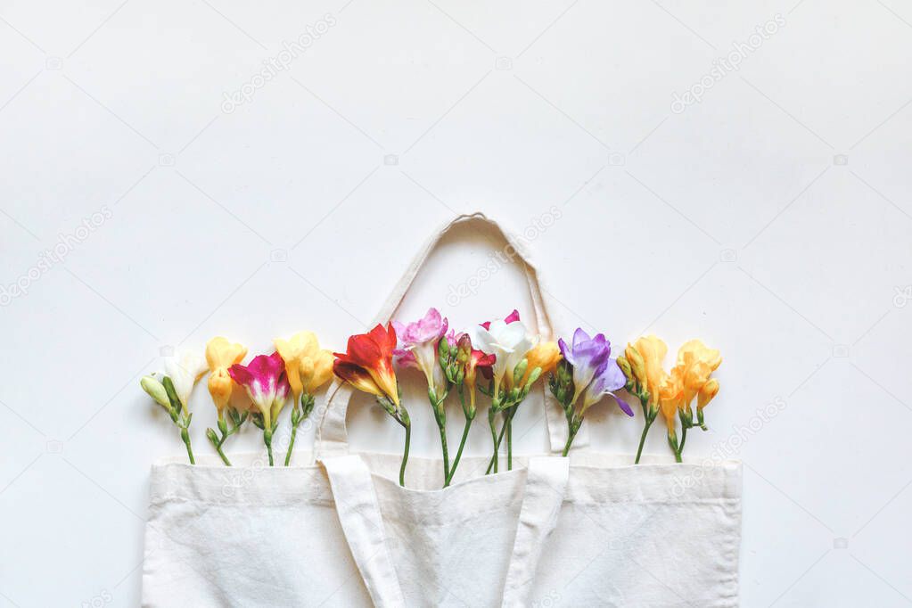 Multicolored freesia flowers in a white canvas bag on a white background
