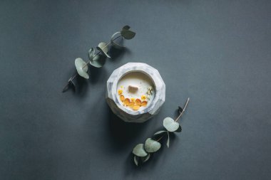 Ekolojik ve vejetaryen el yapımı mum, gri arka planda, betondan yapılmış bir bardakta kuru çiçekler ve yeşil okaliptüs dallarıyla.. 