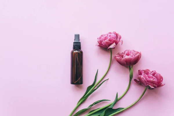 Frascos cosméticos hechos de vidrio ámbar y tulipanes rosados sobre un fondo rosa. — Foto de Stock