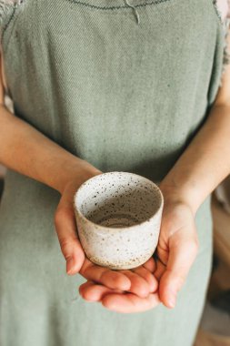 Bir zanaatkar kadın elinde el yapımı bir seramik bardak tutuyor.