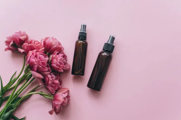 Butelki kosmetyczne wykonane z bursztynowego szkła i różowych tulipanów na różowym tle. — Zdjęcie stockowe