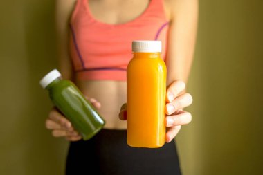 Dişi bir sporcu elinde taze sıkılmış sebze ya da meyve suyu şişeleri tutar..